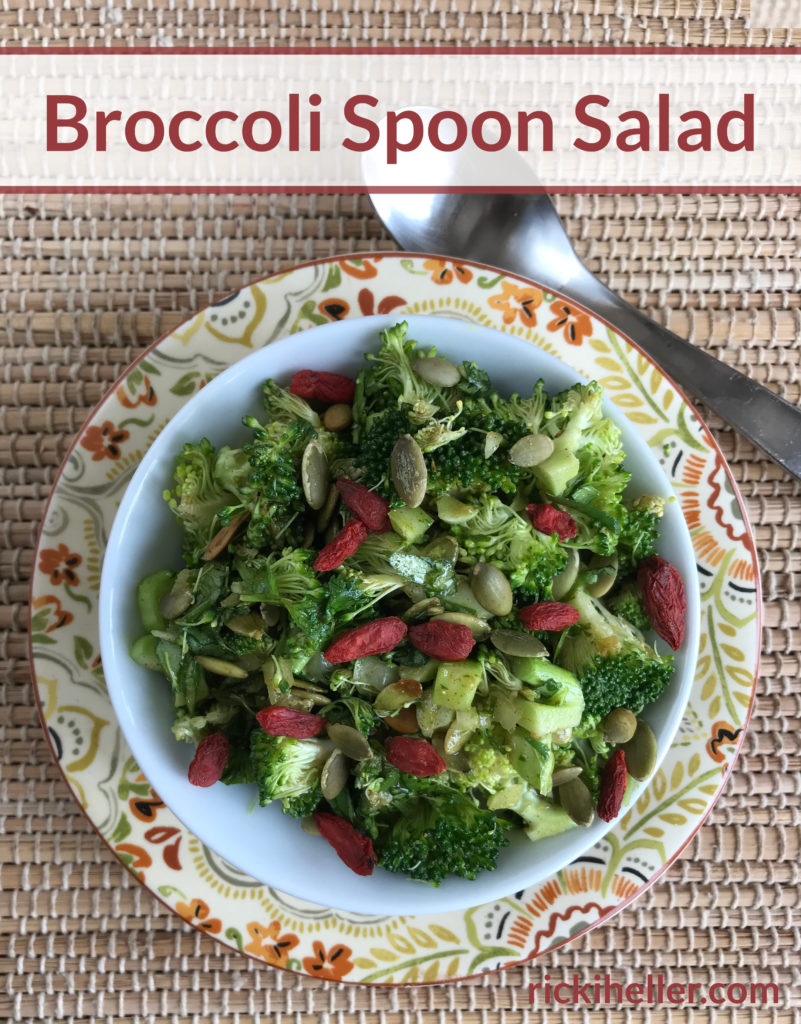 bowl of raw broccoli salad with goji berries and seeds over a colorful plate.